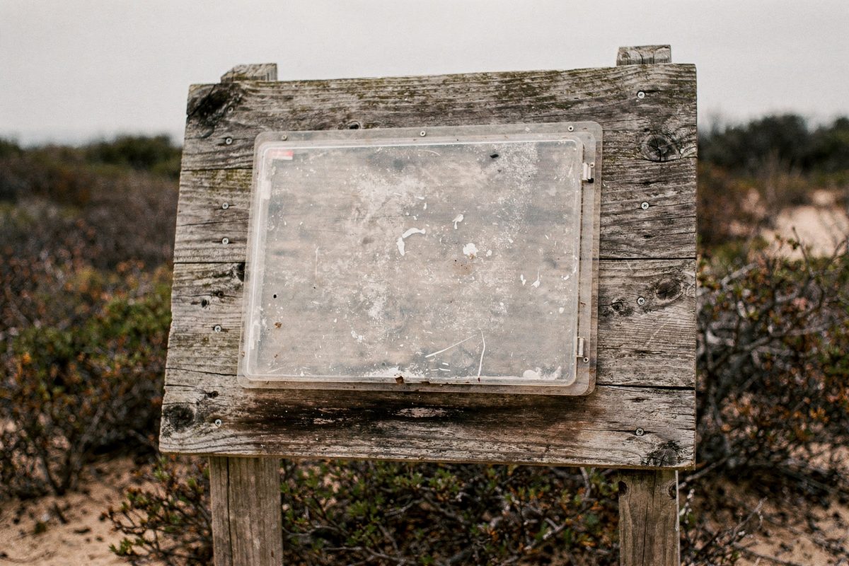 A wooden trailhead kiosk board with an empty plastic map case mounted on it